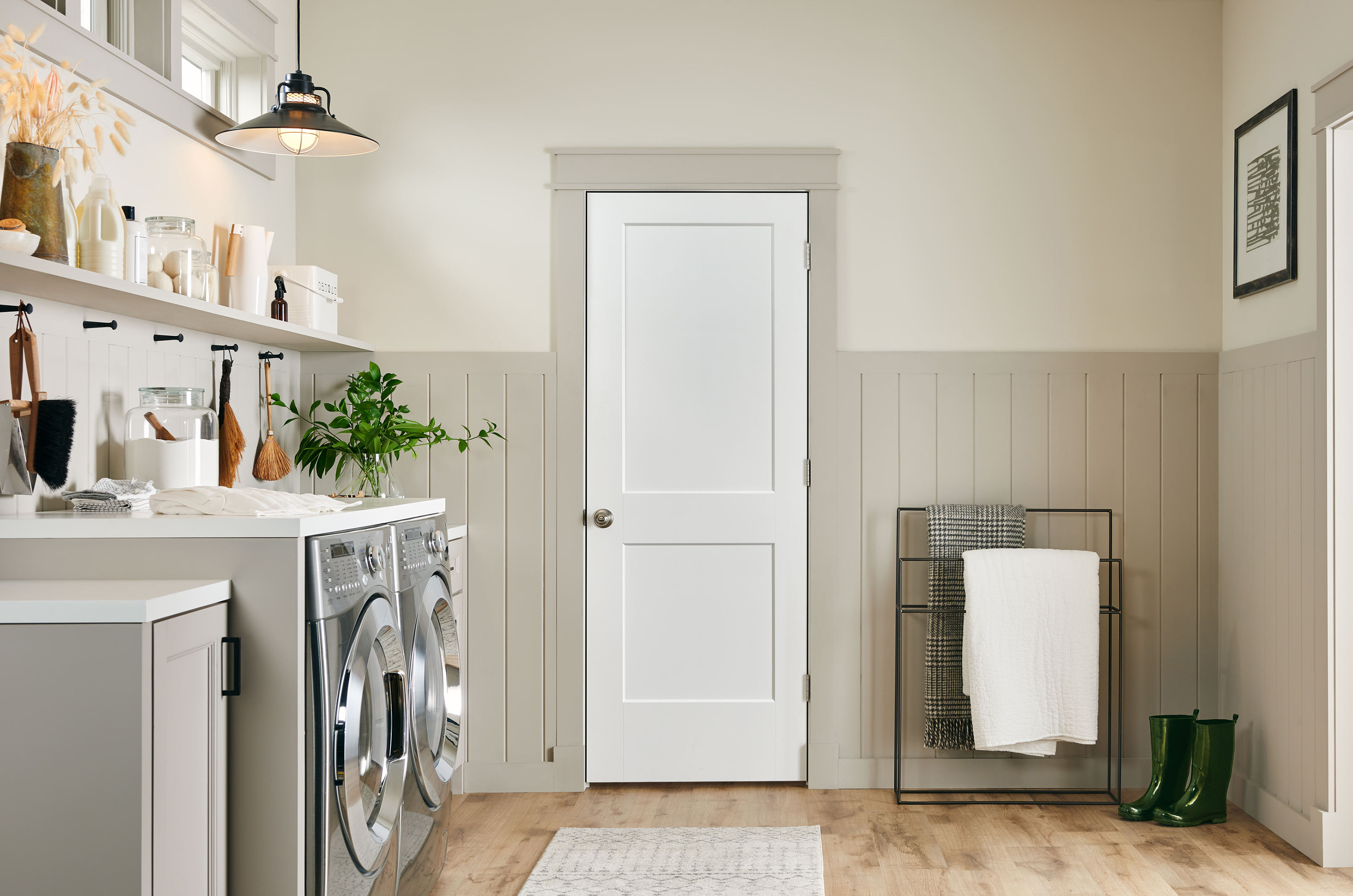 The interior of a transitional-style laundry room with gray wainscotting halfway up and a white two-panel door